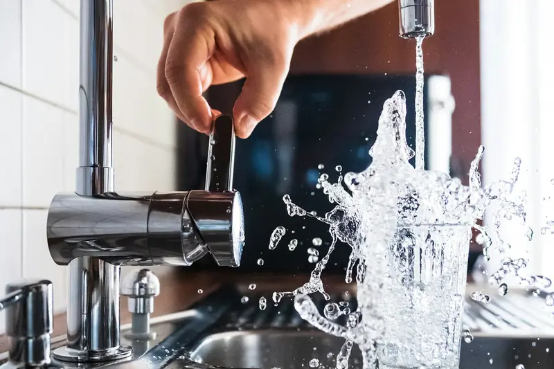 Water spraying out of a kitchen tap over a stainless steel sink