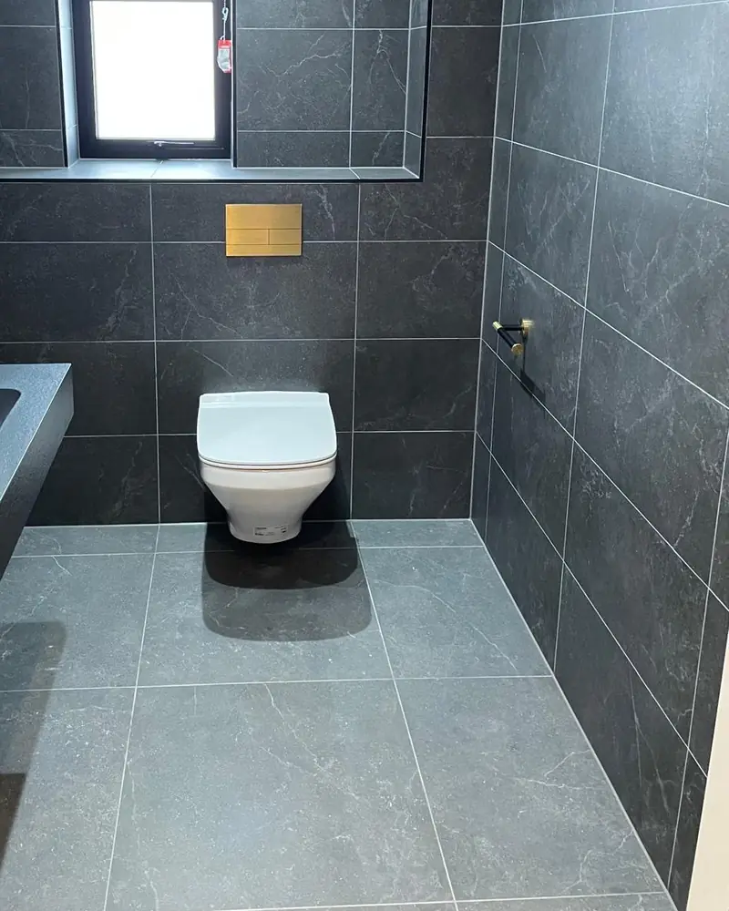 Dark slate-effect cloakroom with a wall-hung toilet and brushed brass flush plate