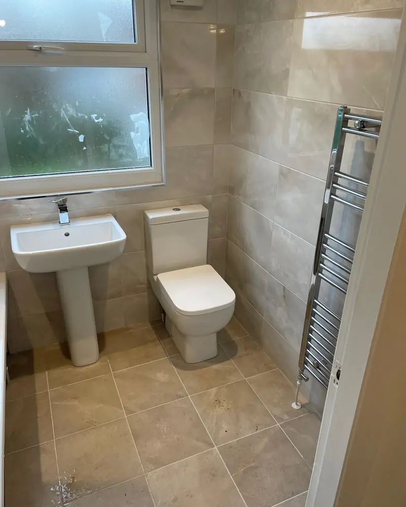 Cream marble-effect bathroom with a pedestal basin, close-coupled toilet and chrome towel rail