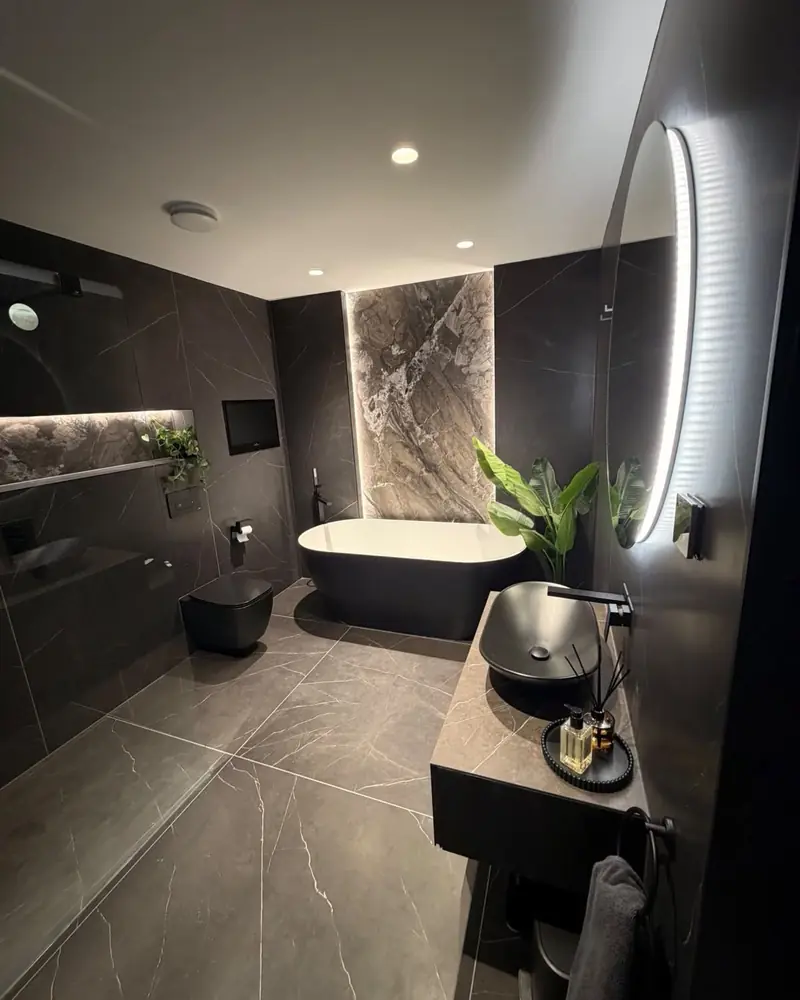 Dark marble-effect bathroom with a black freestanding bath, backlit feature panel and wall-hung toilet