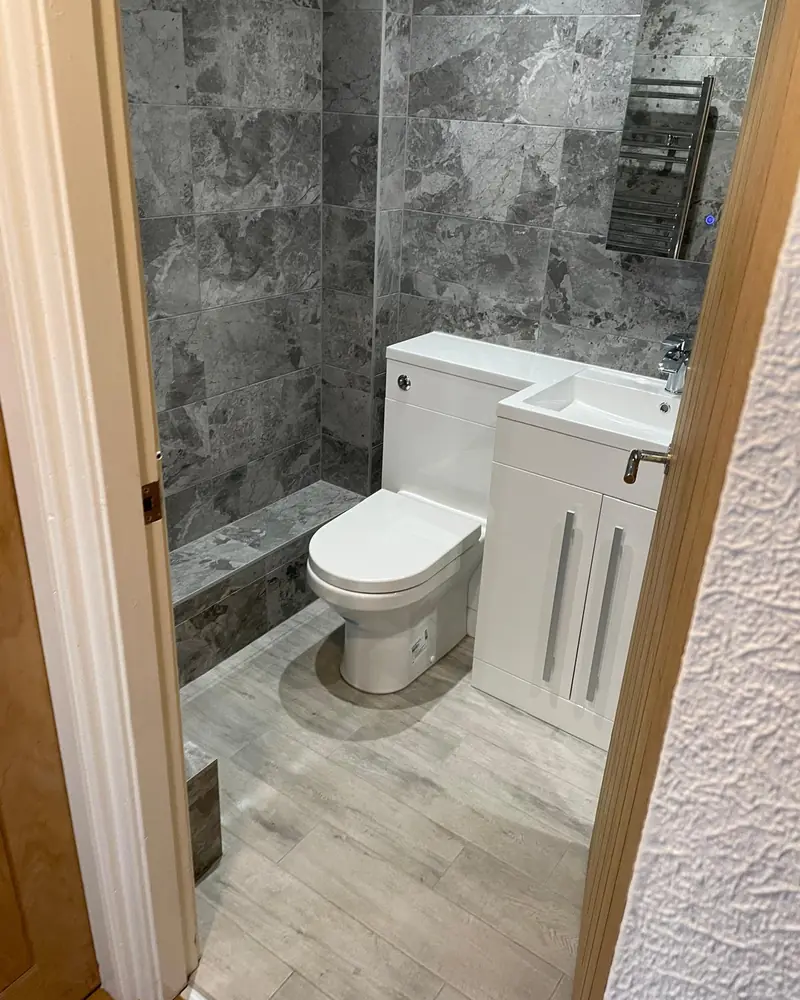 Small grey marble-effect en-suite with a combined toilet and basin unit and a tiled ledge