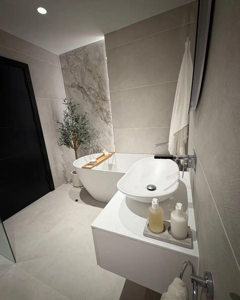 Floating white vanity with a vessel basin, round mirror, wall-hung toilet and lit shelf niche