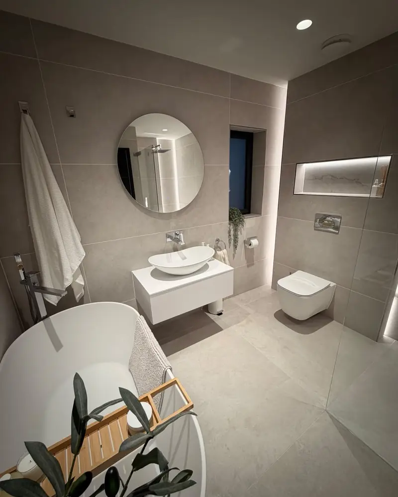 Light grey bathroom with a freestanding bath, backlit marble-effect panel and floating vanity