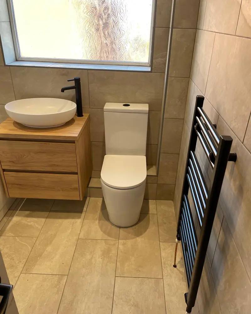 The same bathroom finished, with tiled walls and floor, an oak-effect vanity, toilet and black towel rail