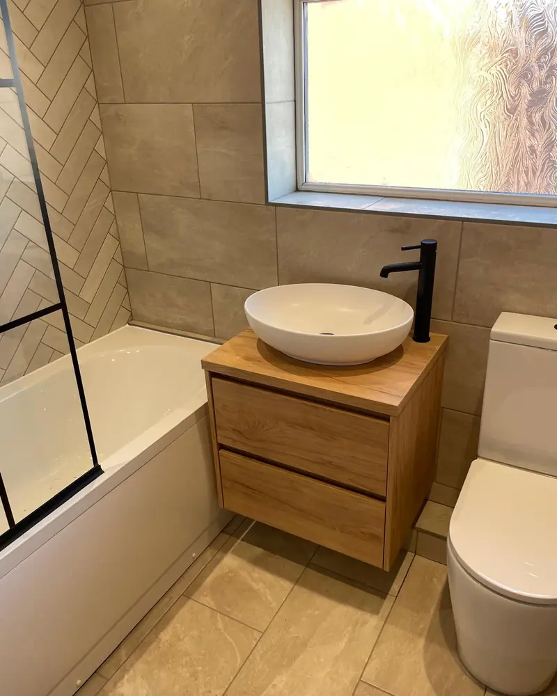 Bathroom with an oak-effect wall-hung vanity, white vessel basin, black tap and a close-coupled toilet under a tiled window reveal