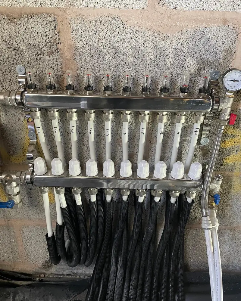 Ten-port underfloor heating manifold with flow meters, numbered loops and a pressure gauge on a block wall