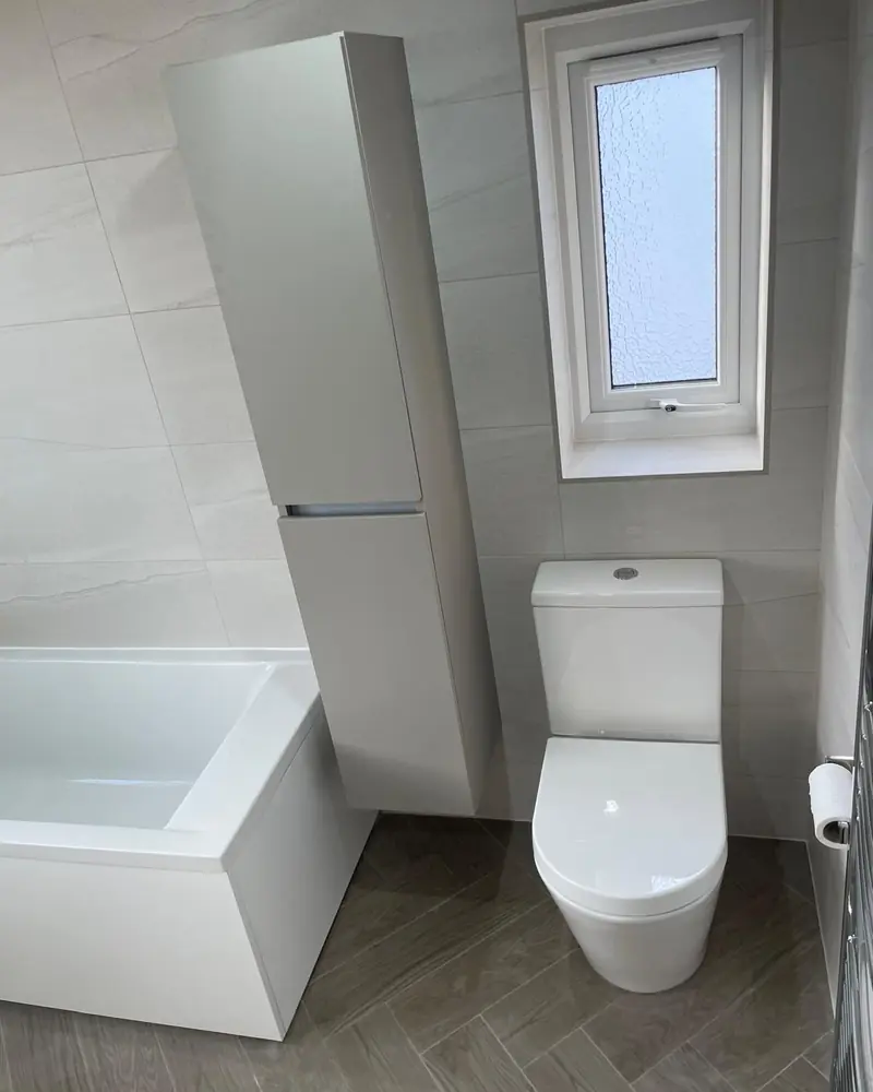 White bathroom with a tall wall-hung storage unit, a close-coupled toilet and herringbone wood-effect floor