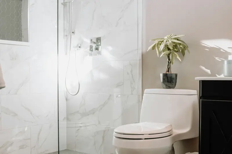 White close-coupled toilet next to a glass shower enclosure in a marble-effect bathroom