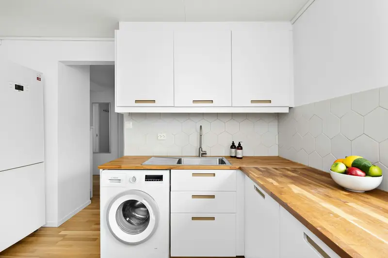 Front-loading washing machine fitted under a wooden worktop in a white kitchen